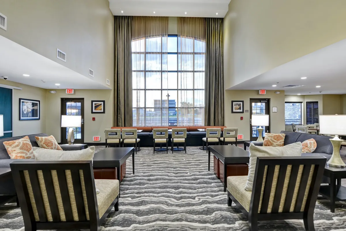 A large window with sheer curtains fills the space with natural light, while comfortable seating areas and stylish coffee tables invite guests to relax, socialize, or read. The decor and soft lighting create a tranquil, inviting atmosphere.