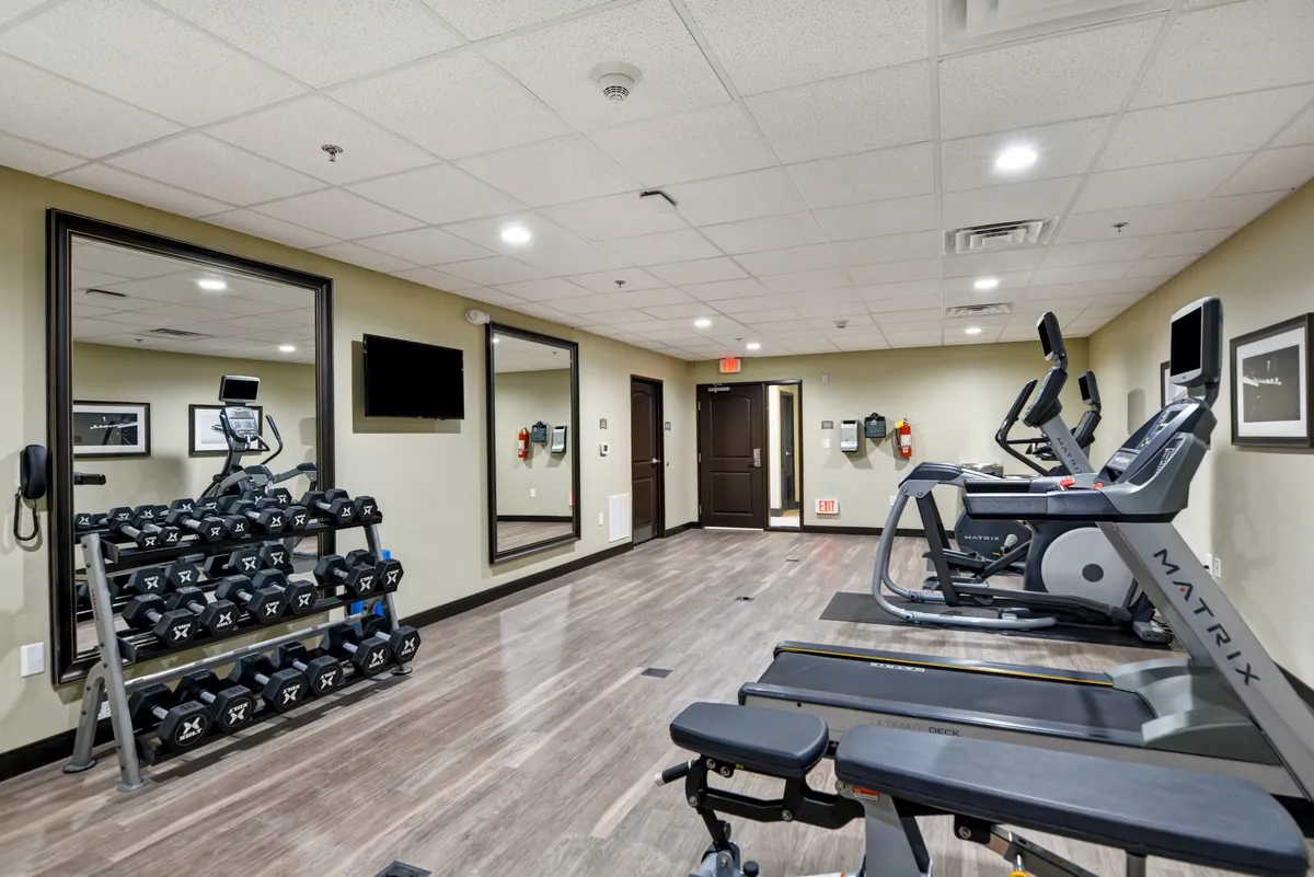 A thoughtfully equipped fitness center featuring a dumbbell rack, multiple exercise machines, large mirrors, and a workout bench. The space feels energetic and ready to support a variety of fitness routines.