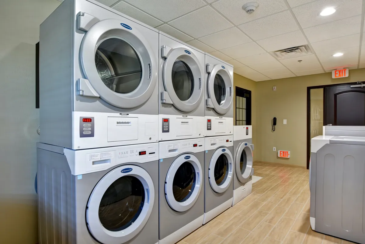 A well-organized laundry facility featuring stacked washing machines and dryers, along with a dedicated laundry folding area. The environment is clean and practical, suggesting ease of use and efficiency for guests.