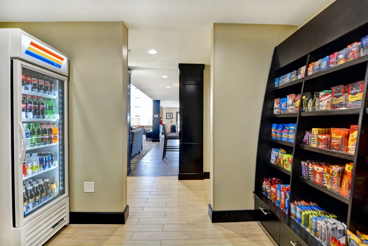 This image showcases a bright, open corridor with a vending machine and snack shelf, suggesting easy access to quick refreshments for residents. The casual lounge area invites socializing and adds to the sense of convenience for those on extended stays.