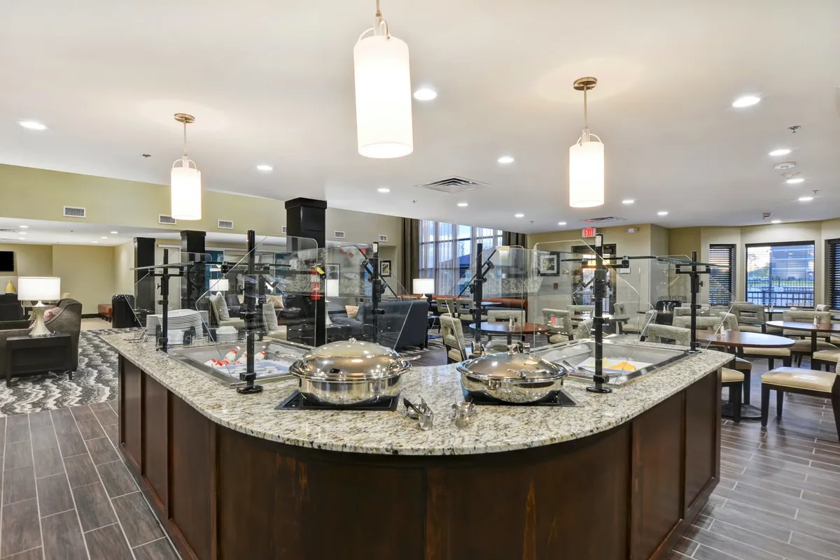 A communal dining space with a granite countertop, serving dishes set out for a meal, hanging light fixtures, and an inviting seating area. The space is set up for shared dining experiences and casual gatherings.